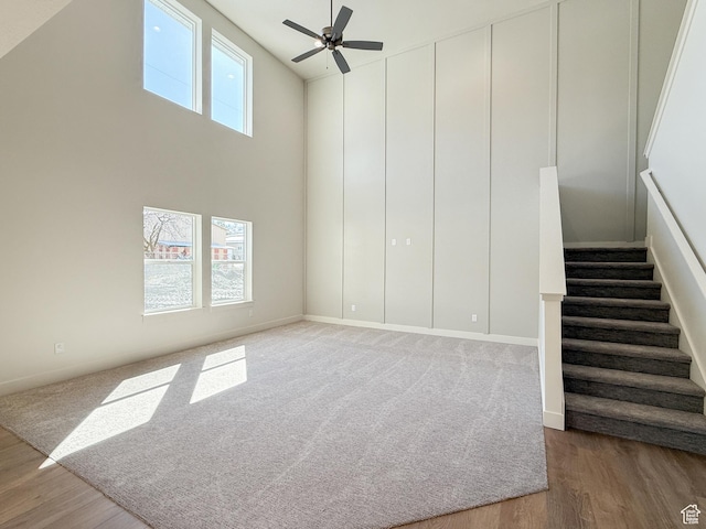 unfurnished living room with stairs, a high ceiling, wood finished floors, and ceiling fan