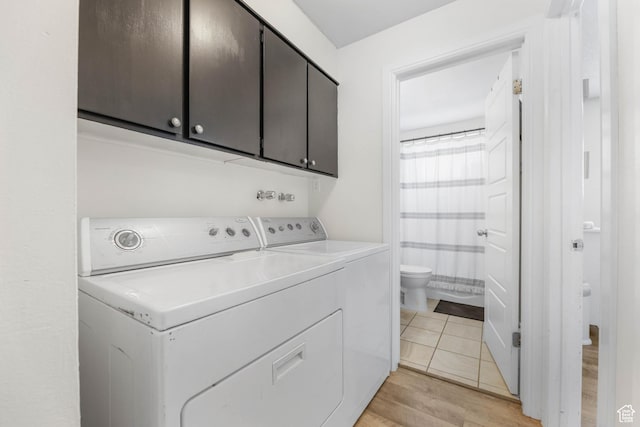 clothes washing area with cabinets, washing machine and dryer, and light wood-type flooring