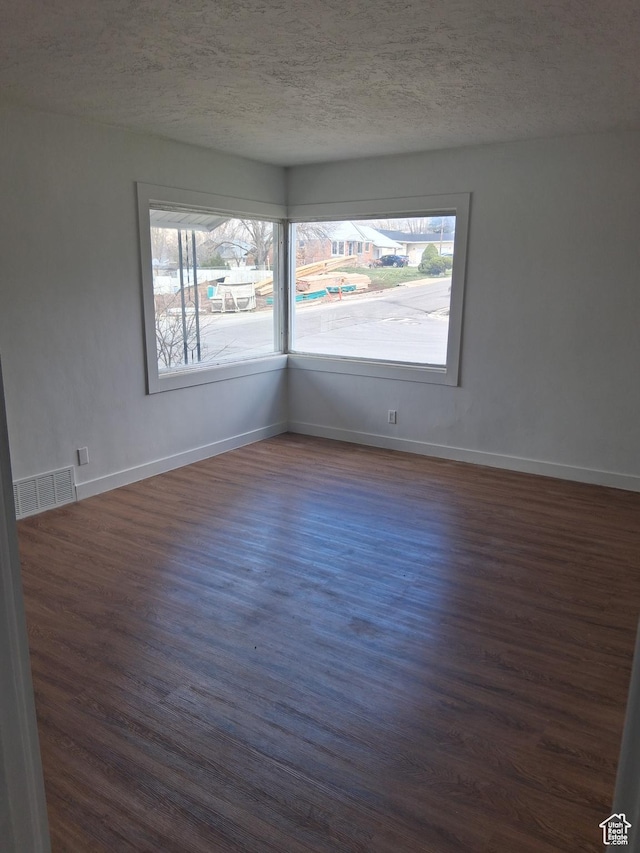 spare room with dark wood finished floors, a wealth of natural light, visible vents, and a textured ceiling