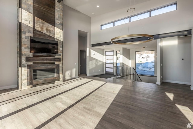 unfurnished living room with an inviting chandelier, a fireplace, a towering ceiling, and wood-type flooring