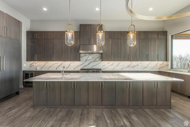 kitchen with hardwood / wood-style flooring, dark brown cabinetry, wine cooler, an island with sink, and decorative backsplash
