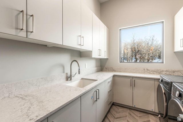 kitchen featuring dark parquet flooring, sink, light stone counters, white cabinetry, and washer and dryer