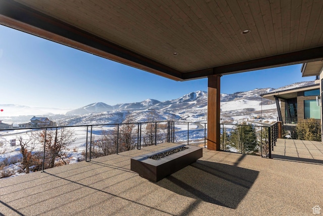 snow covered patio with a mountain view, a balcony, and an outdoor fire pit