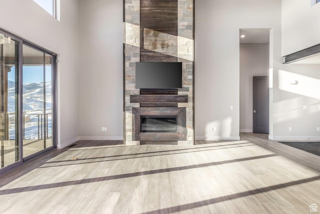 unfurnished living room with a large fireplace, wood-type flooring, a mountain view, and a high ceiling