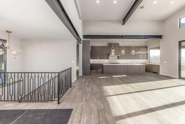 kitchen featuring wall chimney range hood, an inviting chandelier, wood-type flooring, decorative backsplash, and beamed ceiling