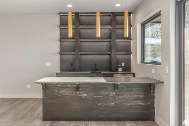bar featuring sink, hanging light fixtures, and light hardwood / wood-style flooring