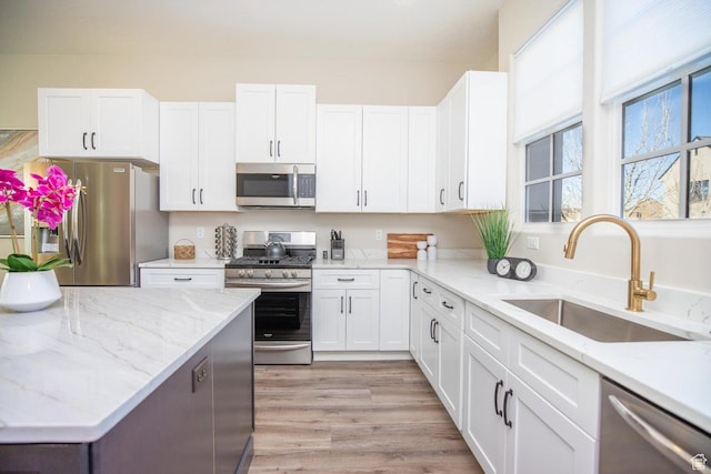 kitchen featuring sink, white cabinetry, stainless steel appliances, light stone countertops, and light wood-type flooring