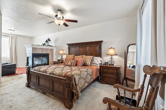 bedroom featuring a ceiling fan, a tile fireplace, light carpet, and a textured ceiling