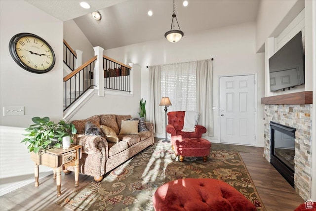 living area with a fireplace, high vaulted ceiling, wood finished floors, and stairs