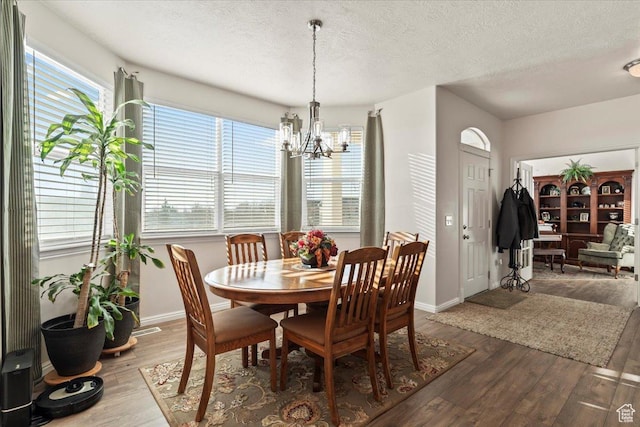 dining space featuring baseboards, a notable chandelier, wood finished floors, and a textured ceiling
