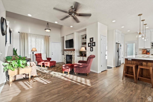living room with a textured ceiling, wood finished floors, ceiling fan, and a stone fireplace