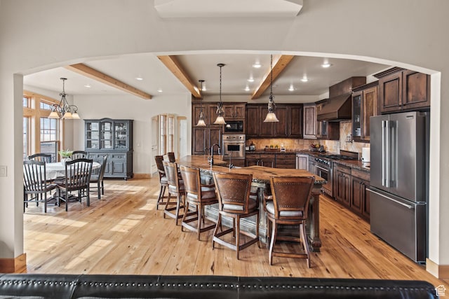 655 W 85 S, Glenwood, UT 84730 - kitchen with premium appliances, wall chimney exhaust hood, beam ceiling, dark brown cabinetry, and light wood finished floors