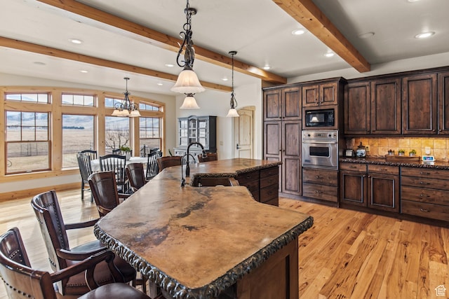 655 W 85 S, Glenwood, UT 84730 - kitchen with oven, light wood finished floors, an island with sink, black microwave, and beamed ceiling