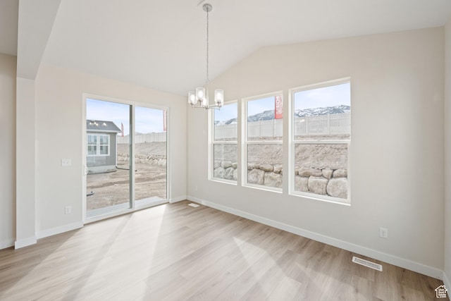unfurnished dining area featuring an inviting chandelier, lofted ceiling, a mountain view, and light wood-type flooring