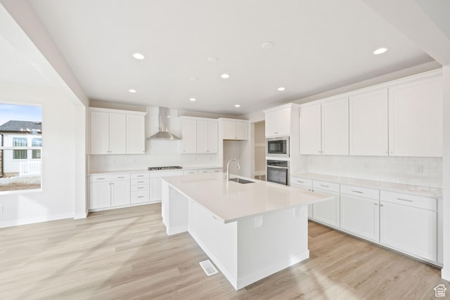 kitchen featuring wall chimney exhaust hood, sink, white cabinetry, stainless steel appliances, and a kitchen island with sink