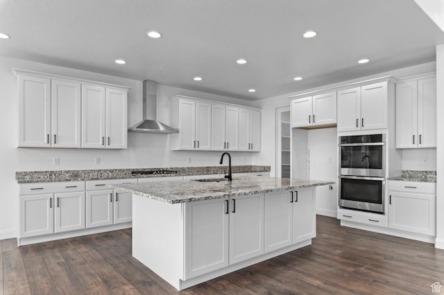 kitchen with sink, white cabinets, stainless steel appliances, a center island with sink, and wall chimney exhaust hood