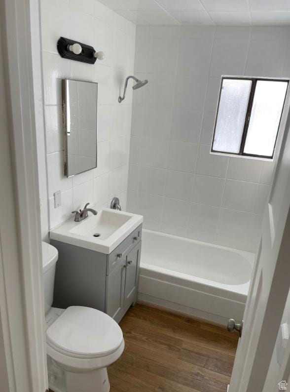 full bathroom featuring toilet, vanity, tiled shower / bath combo, hardwood / wood-style floors, and backsplash