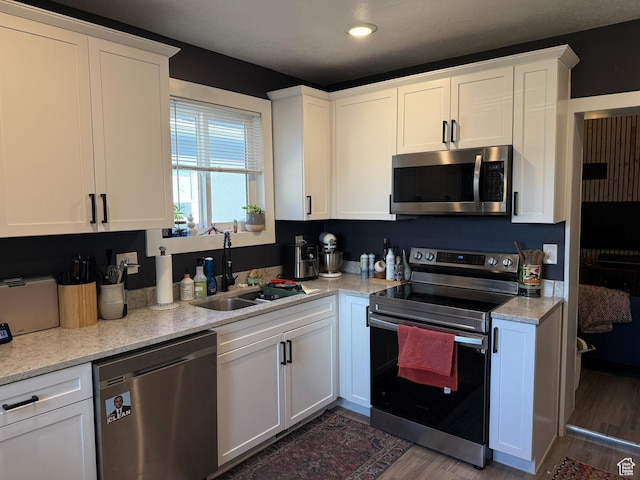 kitchen with sink, dark hardwood / wood-style floors, stainless steel appliances, light stone countertops, and white cabinets
