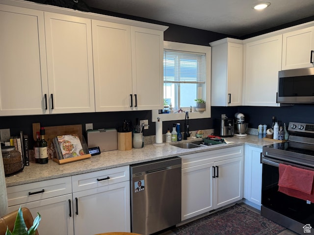 kitchen with stainless steel appliances, light stone countertops, sink, and white cabinets