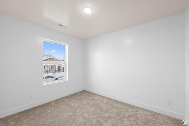 spare room with visible vents, light carpet, baseboards, and a textured ceiling