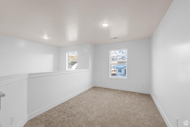 carpeted spare room with baseboards, visible vents, and a textured ceiling