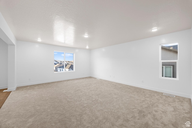 unfurnished room with light carpet, a textured ceiling, visible vents, and baseboards