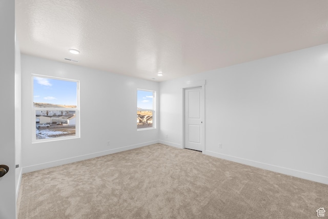 empty room with light colored carpet, visible vents, baseboards, and a textured ceiling