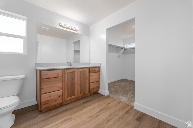 bathroom with baseboards, toilet, wood finished floors, a spacious closet, and vanity