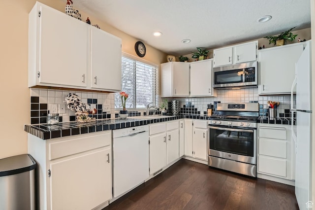 kitchen featuring backsplash, white cabinets, dark hardwood / wood-style flooring, tile counters, and stainless steel appliances