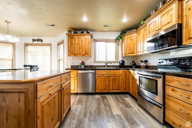 kitchen featuring sink, hardwood / wood-style flooring, hanging light fixtures, stainless steel appliances, and a textured ceiling
