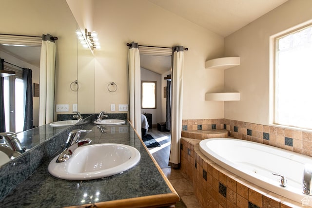 bathroom with vanity, tile patterned flooring, vaulted ceiling, and tiled tub