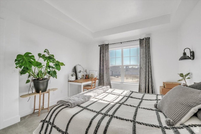 carpeted bedroom featuring baseboards and a raised ceiling