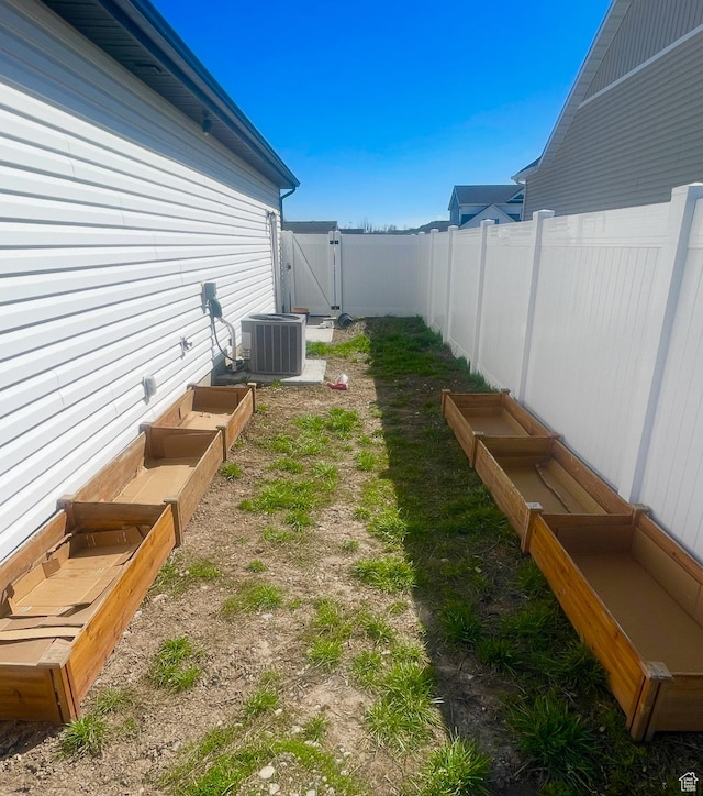 view of yard featuring a vegetable garden, a gate, a fenced backyard, and central AC