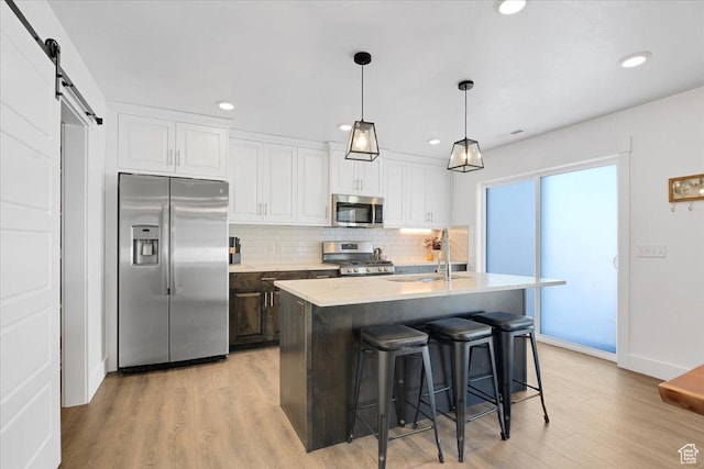 kitchen featuring backsplash, a barn door, appliances with stainless steel finishes, white cabinets, and a sink