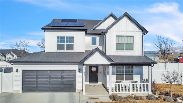 view of front of house featuring roof mounted solar panels, a porch, concrete driveway, and fence