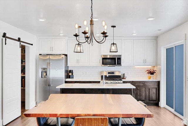 kitchen featuring a kitchen island with sink, stainless steel appliances, light countertops, a barn door, and light wood-type flooring