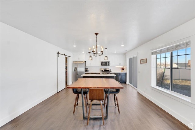 dining space with a barn door, baseboards, wood finished floors, and a chandelier