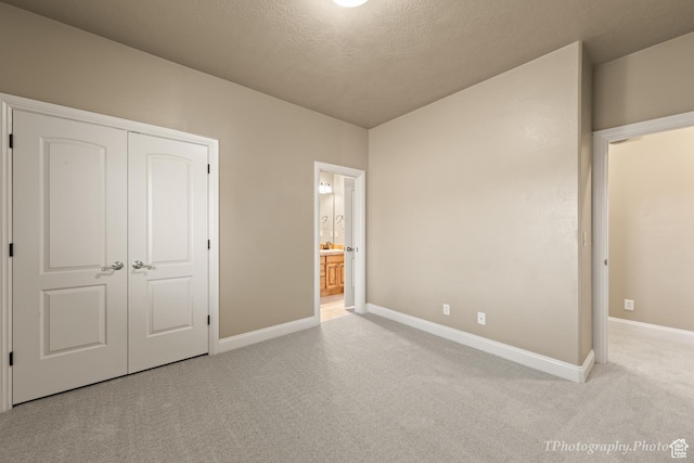 unfurnished bedroom with a closet, connected bathroom, light carpet, and a textured ceiling