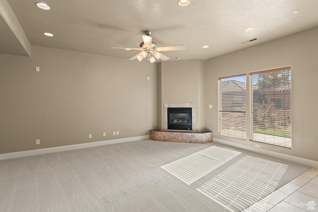 unfurnished living room with ceiling fan, a tiled fireplace, and light colored carpet