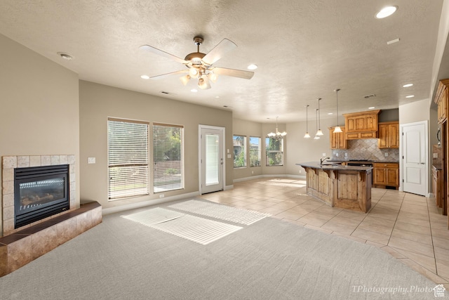 living room featuring light tile patterned flooring, sink, a textured ceiling, a tiled fireplace, and ceiling fan with notable chandelier