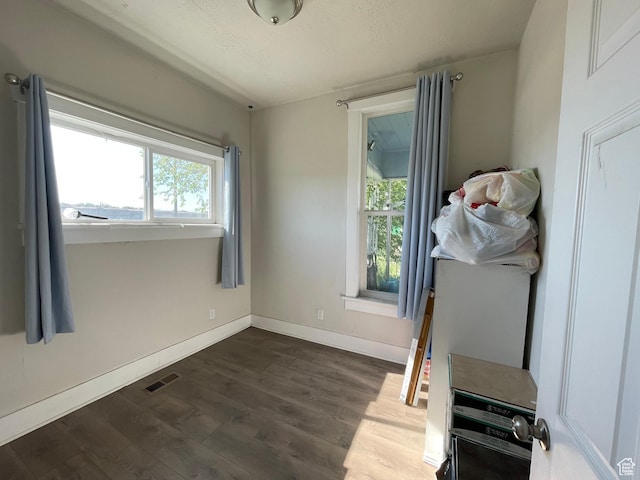 unfurnished bedroom featuring multiple windows, dark wood-style floors, and baseboards