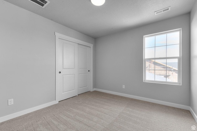 empty room with visible vents, carpet flooring, a textured ceiling, and baseboards