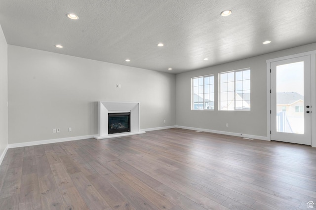 unfurnished living room featuring recessed lighting, baseboards, wood finished floors, and a glass covered fireplace