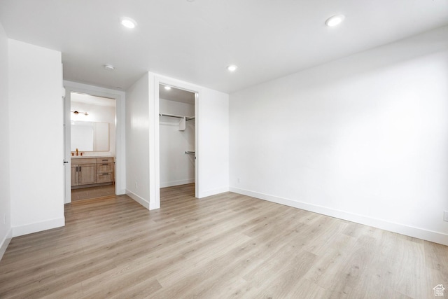 unfurnished bedroom with ensuite bathroom, a spacious closet, a closet, and light hardwood / wood-style flooring