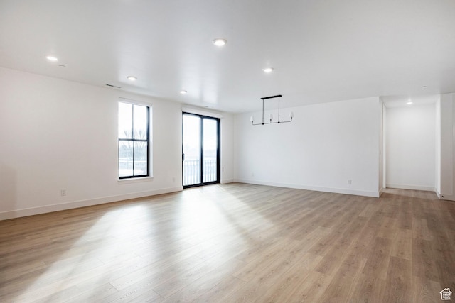 unfurnished room with a notable chandelier and light hardwood / wood-style floors