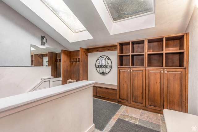 interior space with stone tile flooring and vaulted ceiling with skylight