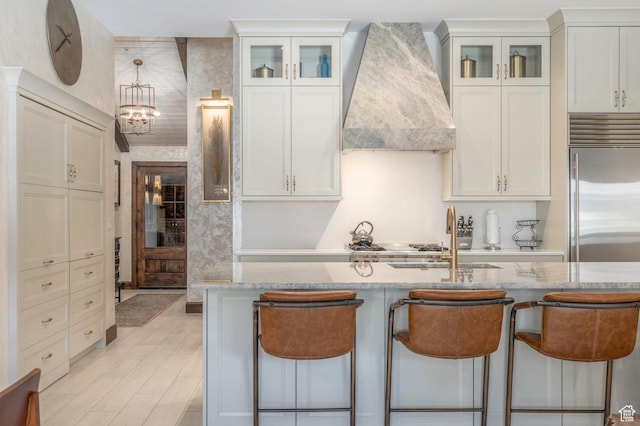 kitchen featuring a breakfast bar area, high end fridge, a sink, light stone counters, and custom exhaust hood