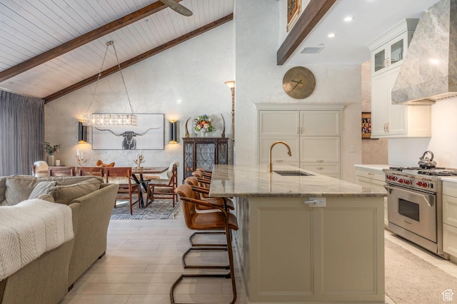 kitchen with beamed ceiling, light stone countertops, luxury range, wall chimney exhaust hood, and a sink