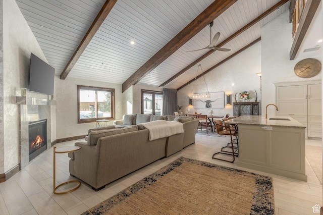 living area with high vaulted ceiling, a fireplace, baseboards, beamed ceiling, and ceiling fan
