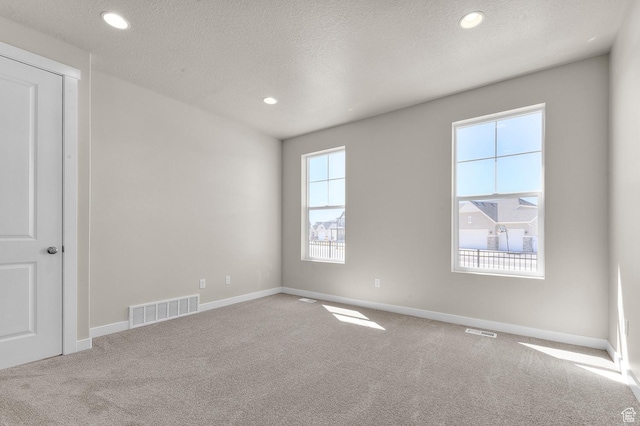 unfurnished room with a textured ceiling, visible vents, and carpet